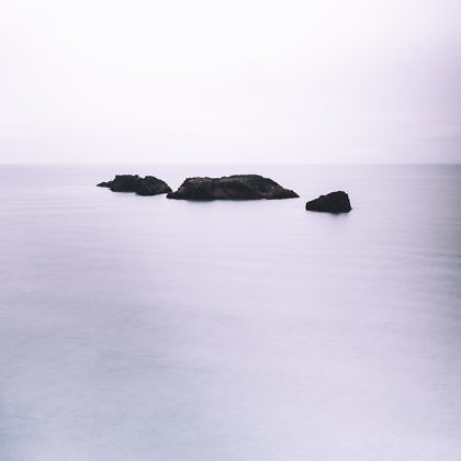 Three small, rocky islands projecting from the ocean, with a light purple haze