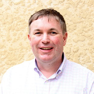 Dr Scott Hollier looking at the camera and smiling. He wears a collared checked shirt.