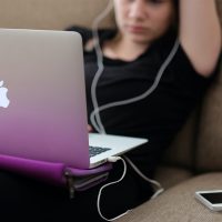 Person sitting on a couch using a Macbook with headphones on.