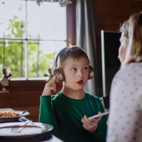 Young child with headphones on holding a smartphone and looking up at a parent.