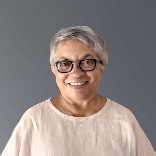 Jackie, wearing glasses and a white shirt, is smiling at the camera.