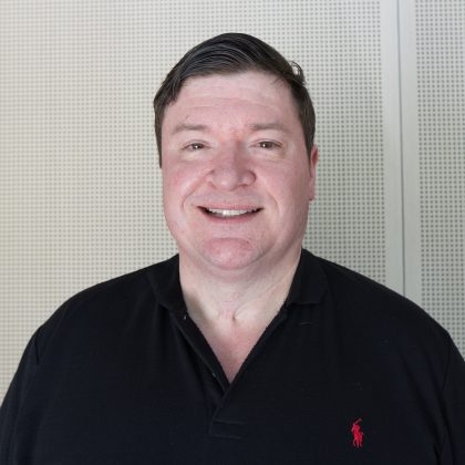 Scott La Vertu beams at the camera. He is wearing a black shirt.