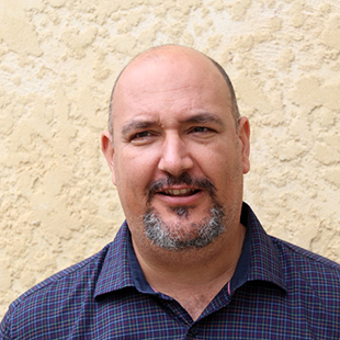 Portrait of Stewart Luxton. Stewart wears a dark blue collared shirt with a light check pattern.