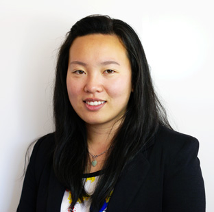 Yumei Lim looking at camera with a subtle smile. She wears a necklace with a jade coloured pendant, a dark blazer and a light shirt.