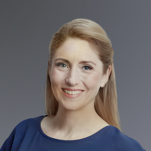 Dawn McAleenan, with long blonde hair, smiles at the camera. She is wearing a blue top.