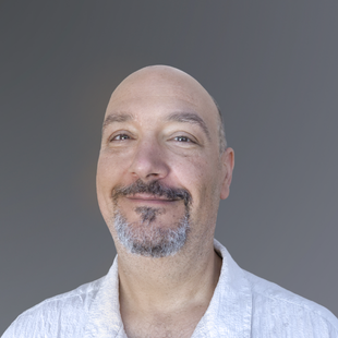 Stewart is smiling at the camera. He is wearing a white collared shirt.