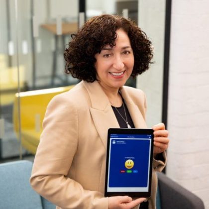 Image of SeamlessCare CEO and co-founder Dr Aviva Cohen, a woman with dark curly hair, holding a mobile device that is displaying the Empathic app.