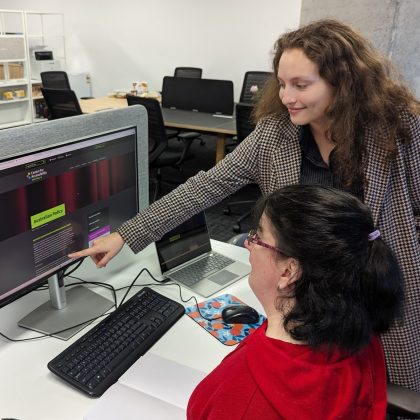 Image of two women, one in a red jumper, the other pointing to a computer.