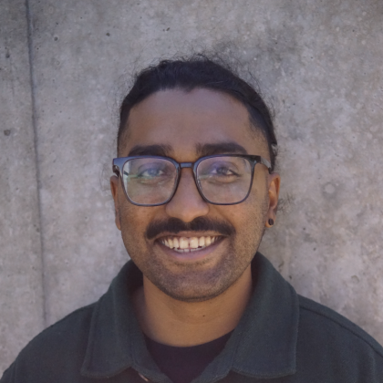 Photo of Bryan Benjamin Man with dark hear wearing glasses with a moustache smiling