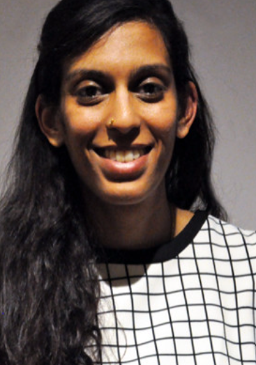 Image is of a smiling woman with long dark hair, wearing a white dress with a black squared pattern. 