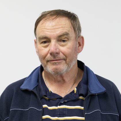 Glenn Wilson smiles at the camera. He is wearing a dark blue jacket, and striped polo shirt.