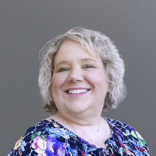 Tamara is wearing a colourful, floral top. She is smiling at the camera.